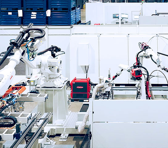 Linea di produzione automatizzata con robot industriali antropomorfi impegnati in operazioni di assemblaggio e saldatura all’interno di un impianto industriale.