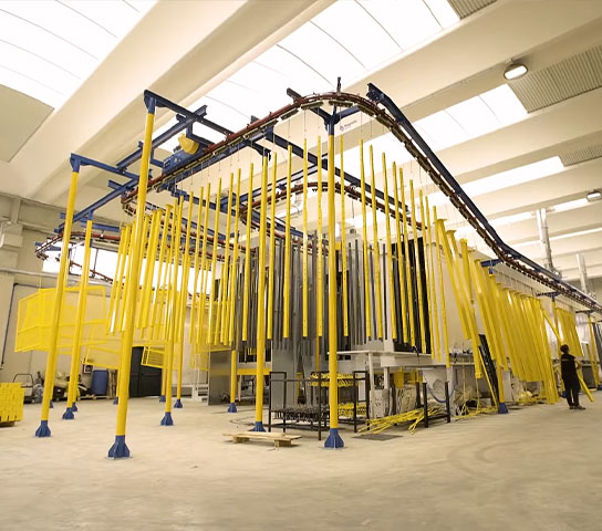 Linea industriale automatizzata per il trattamento superficiale dei metalli, con convogliatore aereo e componenti appesi durante il processo produttivo.